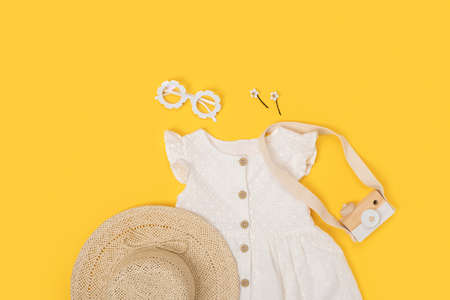 Stylish summer set of child clothes. White dress, straw hat, sunglasses and accessories on yellow background. Fashion girl lookbook concept. Top view Copy space Flat lay.の写真素材