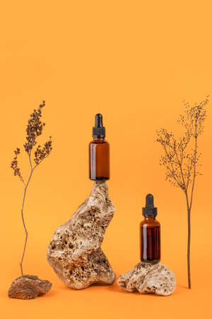 Serum or essential oil in brown glass dropper bottles on stone and dried flowers on orange background. Natural Organic Spa Cosmetic concept Front view.の写真素材
