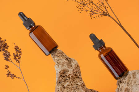 Serum or essential oil in brown glass dropper bottles on stone and dried flowers on orange background. Natural Organic Spa Cosmetic concept Front view.の写真素材
