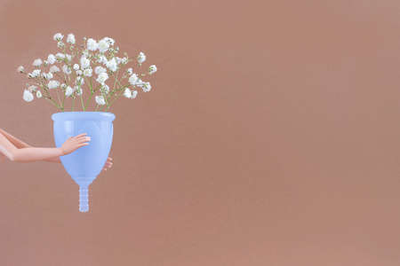 Blue menstrual cup and bouquet delicate flowers on brown background with copy space. Female intimate hygiene. Women health concept, eco-friendly, zero waste alternatives.の写真素材