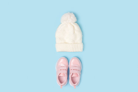 White knitted hat and pink sneakers on blue background. Winter set of child clothes. Fashion kids outfit. Top view Flat lay Minimal style.の写真素材