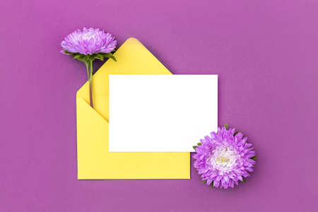 White blank card, yellow envelope and flower on purple background. minimal style. Top view Flat lay Mockup.の写真素材