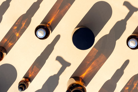 Pattern made with brown glass bottle of cosmetic products and strong shadow on beige background, as a backdrop or texture. Creative layout for your design.の写真素材