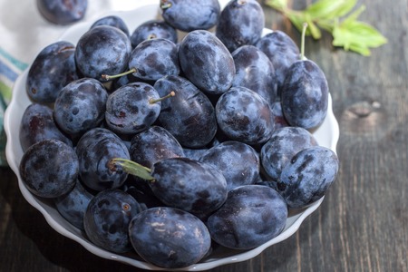Berries plum in a plate on a wooden tableの写真素材