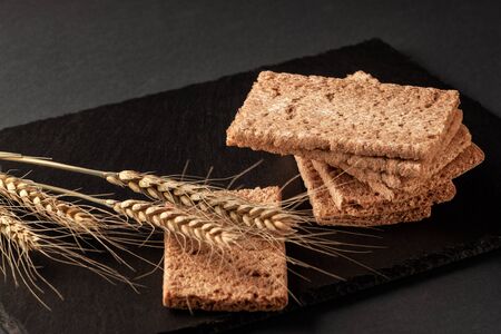 Crispy rye bread with ears of rye lies on a black serving board