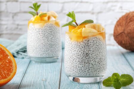 On a blue wooden table, chia pudding with banana in two glass glasses with raw chia seedsの写真素材
