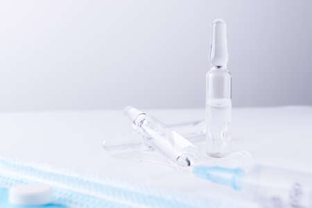 On the white table is a syringe and a row of vials of medicine. Horizontal composition. Foreground.