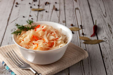 On a wooden table, sauerkraut with carrots and spices in a bowl. Horizontal top view, rustic styleの写真素材
