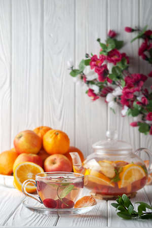 Fruit tea with berries, oranges and mint in a glass teapot on a white wooden backgroundの写真素材
