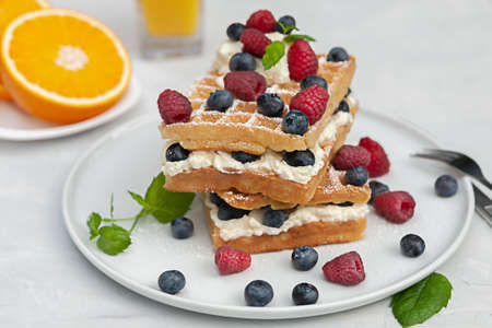 Fresh Viennese or Belgian waffles on a plate with fresh raspberries and blueberries and whipped...