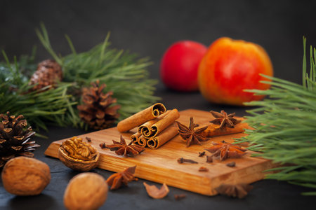 Fragrant cinnamon sticks with anise, apples and nuts on a wooden board on a black background