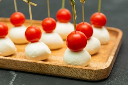 Finger Food snacks and appetizers for buffet. Canapes with mozzarella cheese and cherry tomatoes served on wooden tray.の写真素材