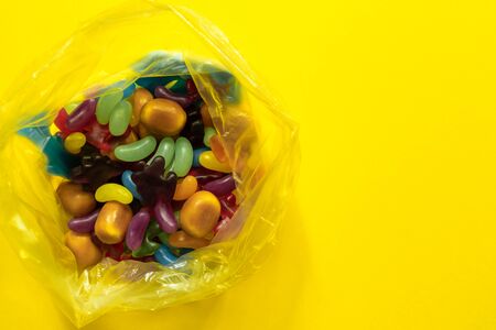 Multi-colored glazed jelly beans sweets in plastic package on yellow paper background.