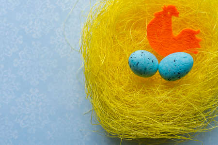 Artificial easter nest with two eggs and cock in blue backgroundの写真素材