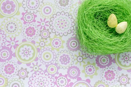Artificial green nest with two eggs on flower background