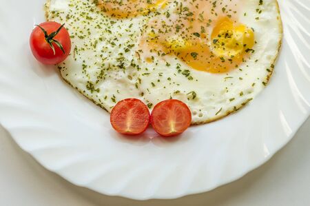 fried eggs on a plate with tomatoes and chopped parsleyの写真素材