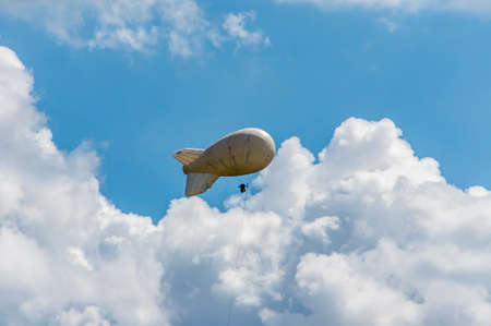 White airship of a soft system with stabilizers and a motor hovers in the skyの写真素材