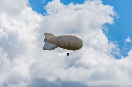 White airship of a soft system with stabilizers and a motor hovers in the skyの写真素材