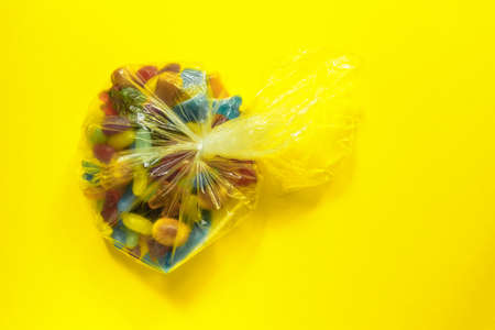 Multi-colored glazed jelly beans sweets in plastic package on yellow paper background.の写真素材