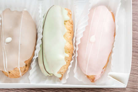 french eclairs in box on wooden table closeup
