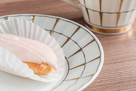 respberry eclair on a plate near tea cup on wooden table