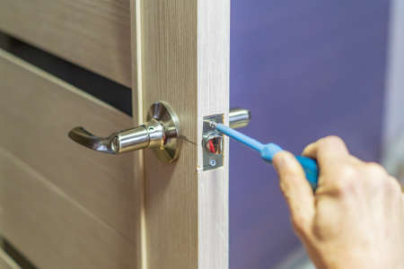 man repairing the doorknob with screwdriver. worker's hand installing new door locker