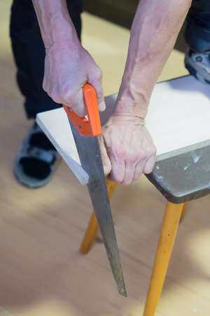man sawing a board with a hacksaw