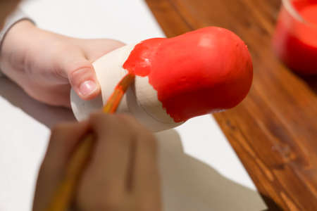 little girl paints russian nesting doll called matrioshka with red paint