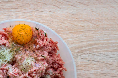 Minced meat in a bowl with raw egg, spices and chopped onion for cooking cutlets, selective focusの写真素材