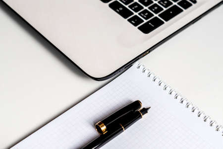 white office desk with white laptop, notebook and fountain pem. Selective focus on pen. の写真素材