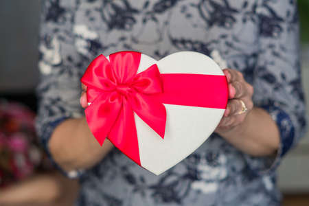 woman holds gift box in a shape of heart with red ribbon