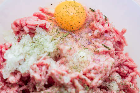 Minced meat in a bowl with raw egg, spices and chopped onion for cooking cutlets, selective focus