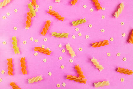 Raw colored fusilli and Stellini pasta scattered on pink background. Top view, flat layの写真素材