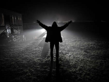 silhouette of man from back side with hands up outdoors against car lights