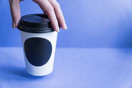 white paper kraft disposable cup for coffee with black plastic lid in a female hand. coffe to go on blue background.の写真素材