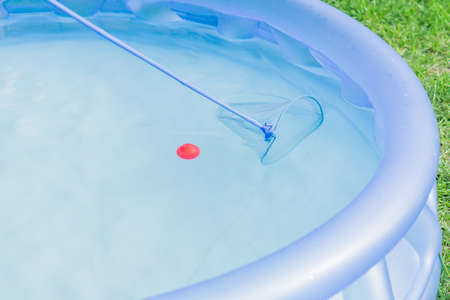 cleaning of garden swimming pool . Boy tries to cach red ball with Skimmer netの写真素材