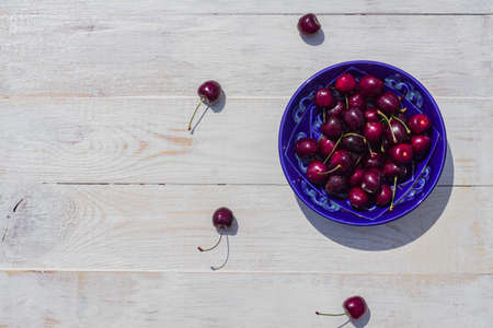 blue plate of ripe sweet cherry on white wooden tableの写真素材