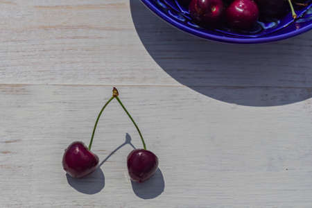 blue plate of ripe sweet cherry on white wooden table