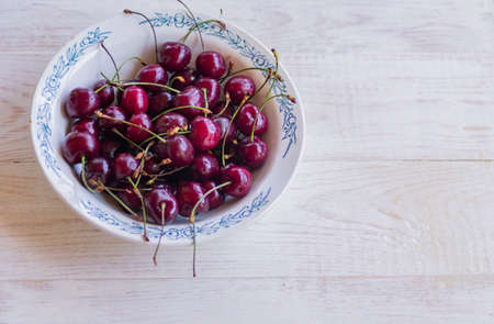 top view of cherry in rustic white plate on wooden table.