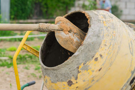 construction worker shovels the sand into rotating concrete mixer. process of creating cement on the...