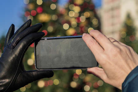 woman hands holding black smartphone fot taking picture of christmas city in a sunny dayの写真素材