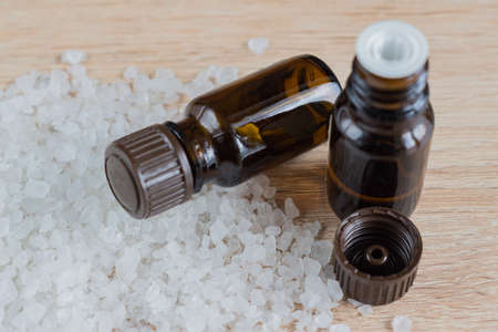 Pile of sea salt and bottles with aromatic oil on wooden table. Natural ingredient for spa and...