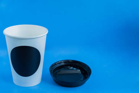 close up of white paper kraft disposable cup for coffee with black plastic lid on blue background with copy spaceの写真素材