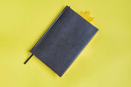 False reptile leather notebook of black color with maple leaf as bookmark on yellow background....