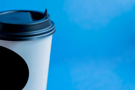close up of white paper kraft disposable cup for coffee with black plastic lid on blue background with copy spaceの写真素材