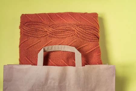 Orange woman warm sweater in paper craft package on yellow background. Clothing sale and black...