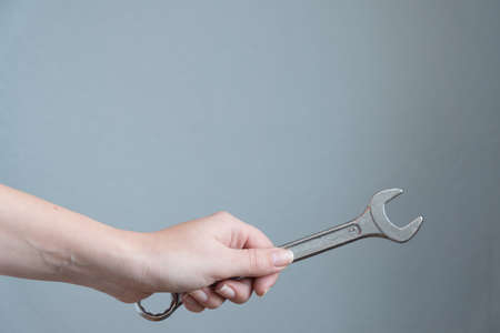 woman holding a wrench in her hand on gray background.