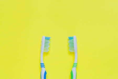 Two toothbrushes on yellow background. Top view, minimal flat lay.