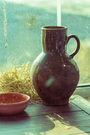 Old clay ceramic jar and clay bowl on wooden table near the window. Rustic still life.の写真素材