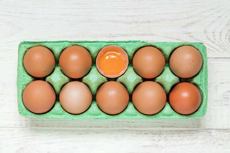 top view of green carton egg box full of raw fresh brown chicken eggs and egg yolk on wooden backgroundの写真素材